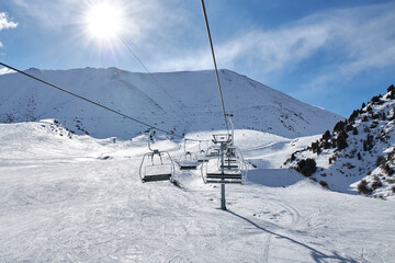 Fototapeta na wymiar Chunkurchak ski resort in Kyrgyzstan. Empty ski lift seats. Mountain slope at sunny winter day, blue sky. Active recreation skiing and snowboarding. Support pillar, Cable car ride.
