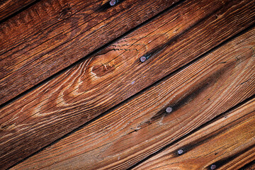 Obraz premium Brązowe chropowate drewniane deski przybite gwoździami z widocznymi słojami i sękami ułożone ukośnie – tło, tekstura