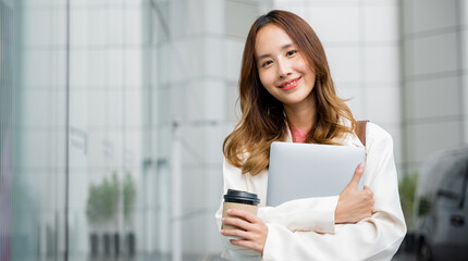 Smiling brunette girl walks down the street, carrying a paper cup of hot coffee and a laptop in her...