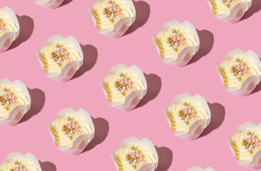 Pattern made from cupcakes with cream and decorating on pink background. Sweet food pattern.