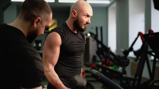 The coach monitors the correctness of the student's exercise with dumbbells in the gym. Bodybuilding classes on special equipment.