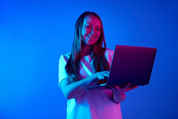 Attractive young woman, holds online meeting using laptop against gradient blue studio background...