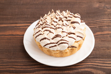 Tartlets with meringue cream and cup of coffee on brown wooden, side view.