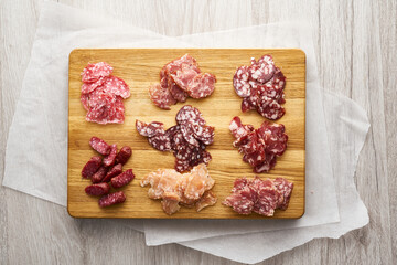 Smoked and dried sausage, cut into thin slices, lies on a wooden stand.