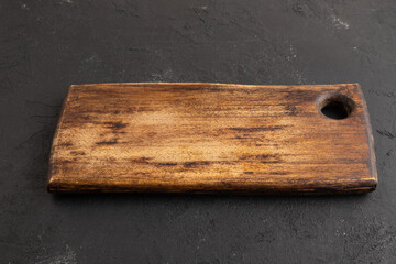 Empty rectangular wooden cutting board on black concrete. Side view