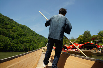 A boatman is punting a river in the Arashiyama area in Kyoto, Japan.