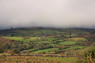 Landscape at rural County Sligo in wintertime featuring rolling hills of farmland pastures bordered by dry stone walls and trees under low lying cloud