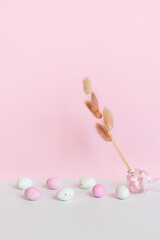 Small speckled white and pink chocolate eggs set on a pastel background, bouquet of dry colors. Easter card with space for text.