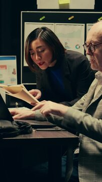 Vertical Video Law agents studying old classified information from police archives folders, looking for clues and crime trends. Partners accessing additional archived resources in incident room