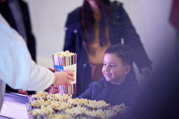 A young boy buys popcorn at the cinema before the start of the movie, his face lit up with excitement.