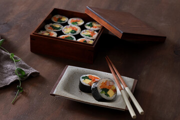 Obraz na płótnie Canvas Kimbap set in a wooden box with chopsticks on a wooden background