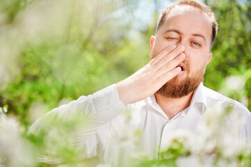 Man allergic suffering from seasonal allergy at spring in blossoming garden at springtime. Close up...