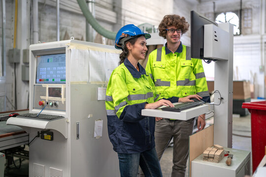 Industrial engineer wear helmet and safety uniform working in heavy engineering factory. Confident technician woman and colleague worker operating automated machine in manufacturing facility workshop