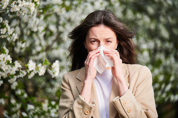 Woman allergic suffering from seasonal allergy at spring in blossoming garden at springtime. Young...