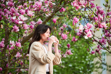 Woman allergic suffering from seasonal allergy at spring in blossoming garden at springtime. Young...