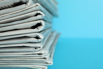 Stack of newspapers on light blue background, closeup with space for text. Journalist's work