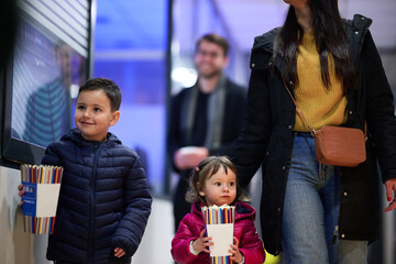 A young couple with their children stands outside the cinema, purchasing freshly popped popcorn before the start of the movie and entry into the theater © .shock