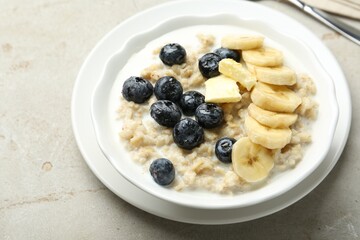 Tasty oatmeal with banana, blueberries, butter and milk served in bowl on light grey table