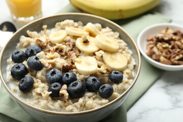 Tasty oatmeal with banana, blueberries, walnuts and milk served in bowl on white marble table, closeup