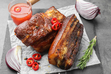 Pieces of baked pork belly served with sauce, rosemary and chili pepper on grey table