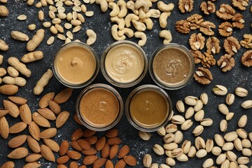 Tasty nut butters in jars and raw nuts on dark gray table, flat lay