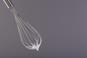 Whisk with whipped cream on grey background. Space for text
