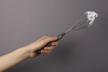 Woman holding whisk with whipped cream on grey background, closeup