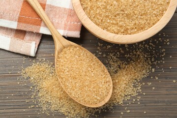 Brown sugar in bowl and spoon on wooden table, flat lay