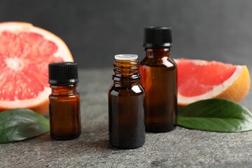Grapefruit essential oil in bottles, leaves and fruit on dark textured table, closeup