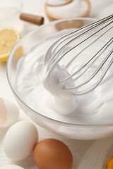 Bowl with whipped cream, whisk and ingredients on white wooden table, closeup