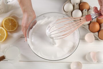 Woman making whipped cream with whisk at white wooden table, above view