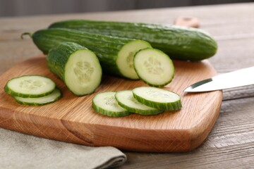 Cucumbers, knife and cutting board on wooden table, closeup