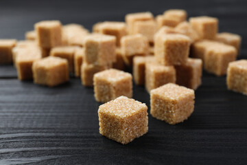 Brown sugar cubes on black wooden table, closeup