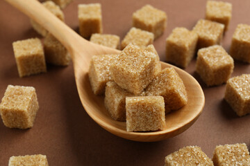 Brown sugar cubes and spoon on color background, closeup