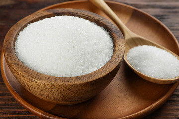 Granulated sugar in bowl and spoon on wooden table, closeup