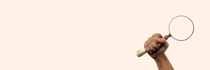 Black male hand holding a magnifying glass isolated on light peach banner.