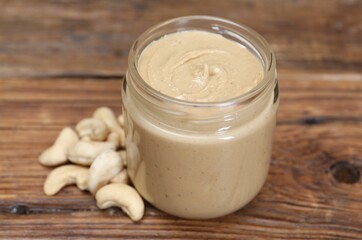 Obraz na płótnie Canvas Tasty nut paste in jar and cashews on wooden table, closeup