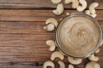 Tasty cashew nut paste in jar on wooden table, top view. Space for text