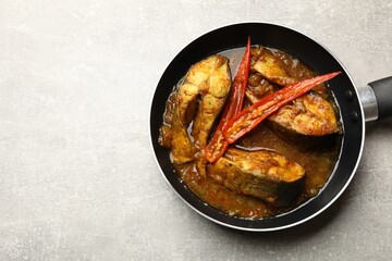 Tasty fish curry in frying pan on light grey table, above view. Space for text. Indian cuisine