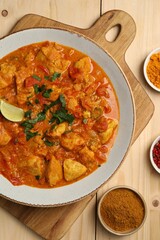 Delicious chicken curry and spices on wooden table, flat lay