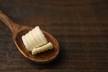 Tasty butter curl and spoon on wooden table, closeup. Space for text