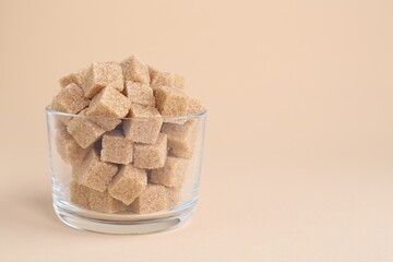 Brown sugar cubes in glass on beige background, closeup. Space for text