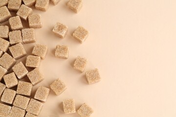 Brown sugar cubes on beige background, top view. Space for text