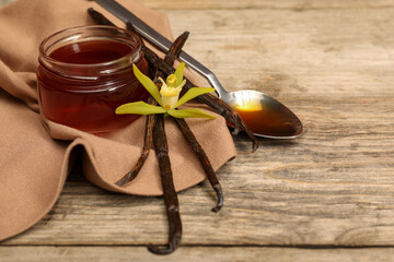 Aromatic vanilla extract, pods and flower on wooden table. Space for text