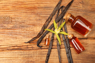 Aromatic vanilla extract, pods and flower on wooden table, flat lay. Space for text