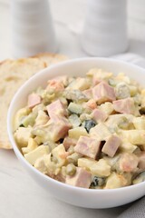 Tasty Olivier salad with boiled sausage in bowl on white table, closeup