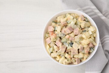 Tasty Olivier salad with boiled sausage in bowl on white wooden table, top view. Space for text