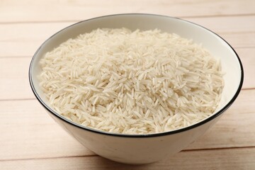 Raw basmati rice in bowl on white wooden table, closeup
