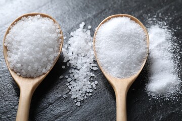 Organic salt in spoons on black table, closeup