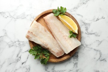 Fresh raw cod fillets with parsley and lemon on white marble table, top view